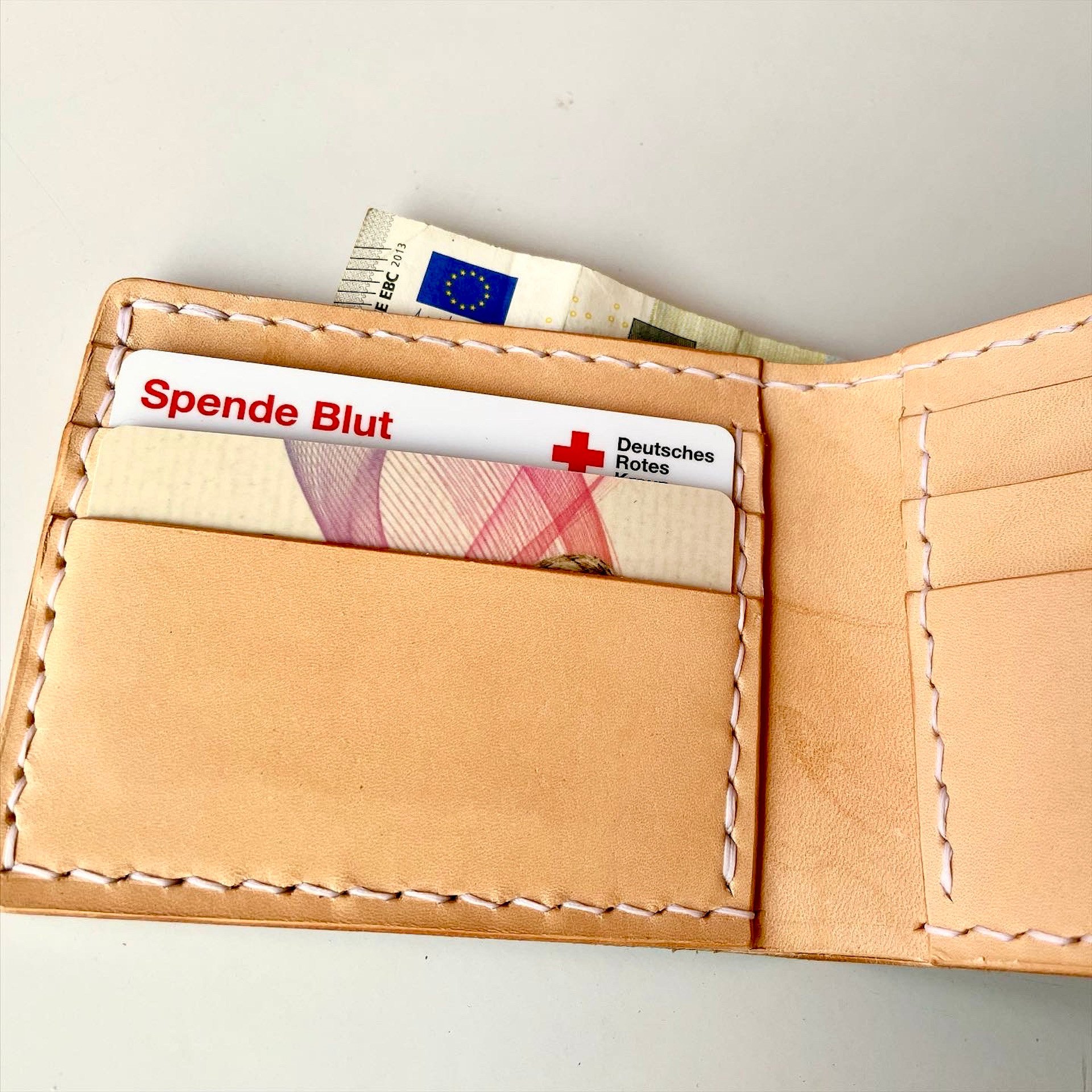 Inside the Wave Wallet by 1985 Studio: a card in the front slot and a banknote in the pocket behind, all in natural vegetable-tanned leather