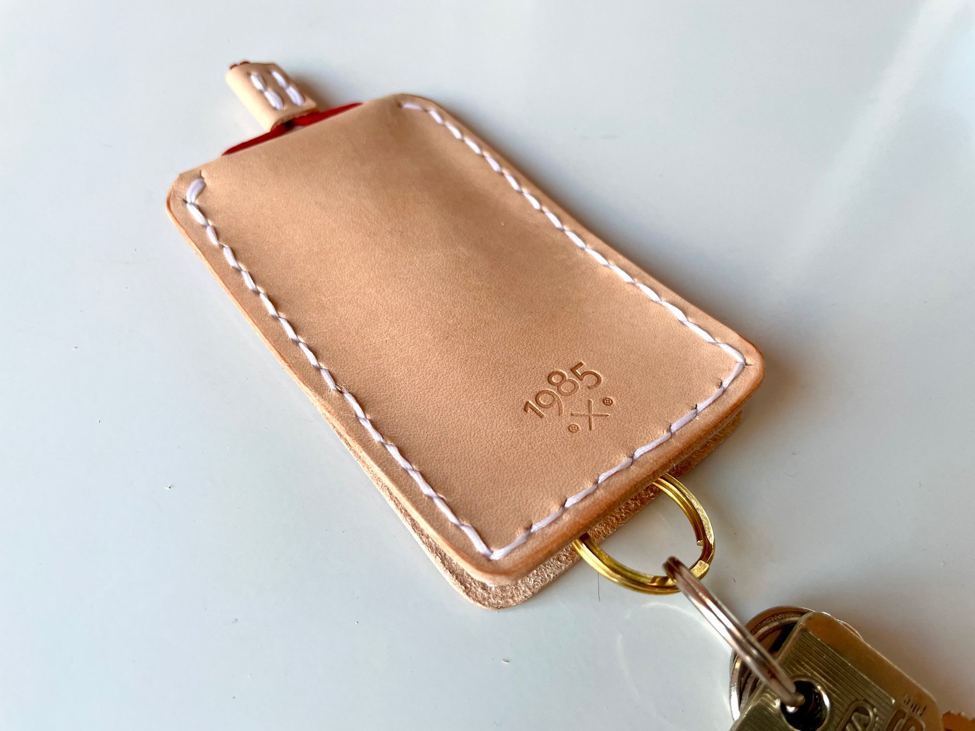 Slim key case by 1985 Studio from above, its sleeve of vegetable-tanned leather with a brass split ring with keys coming out of its lower end