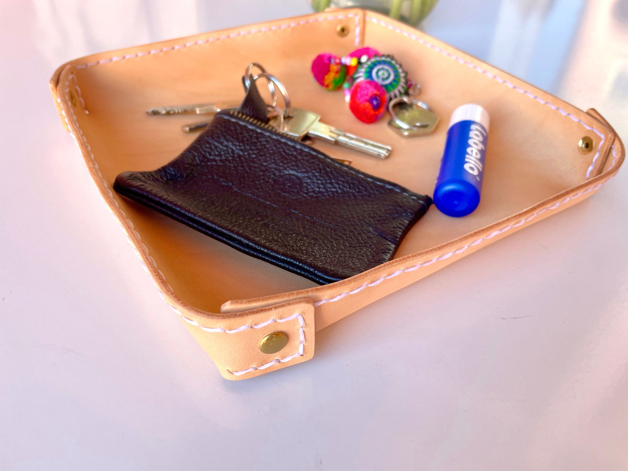 Fold-over valet tray by 1985 Studio in vegetable-tanned leather, holding keys, a black zip pouch, a lip balm and a colorful key charm