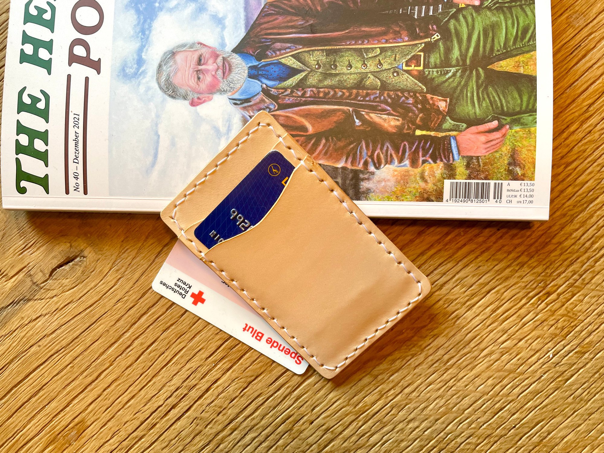 Vertical card wallet by 1985 Studio lying on a magazine on a wooden table, cards in its slot of vegetable-tanned leather