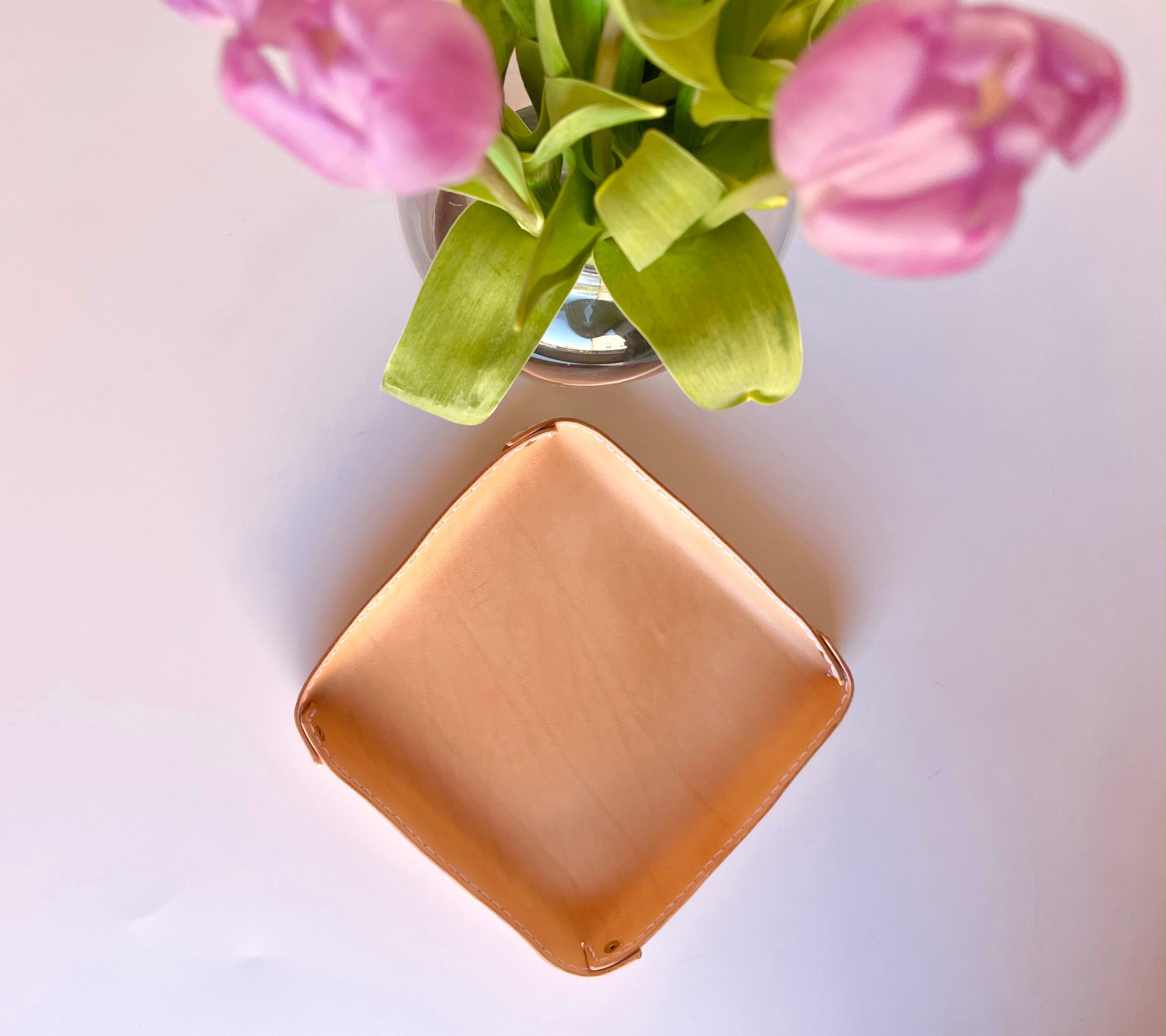 Quadratische, gefaltete Ablageschale von 1985 Studio aus pflanzlich gegerbtem Leder, die Ecken mit Messingnieten aufgestellt, unter einer Vase mit rosa Tulpen