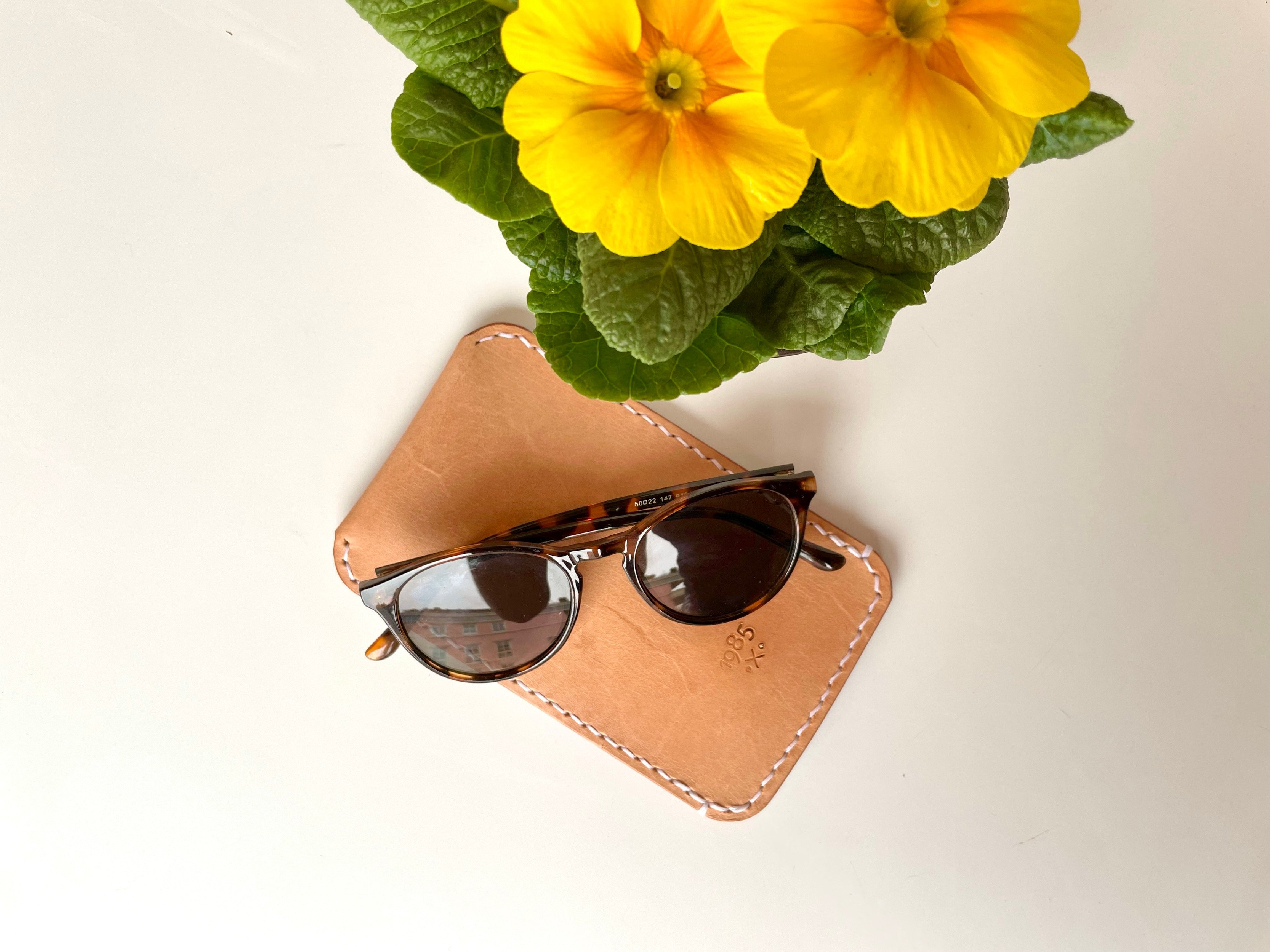 Schmales Sonnenbrillen-Etui von 1985 Studio aus pflanzlich gegerbtem Leder, von Hand im Sattlerstich mit hellem Faden genäht und mit der Marke 1985 geprägt, darauf eine Sonnenbrille