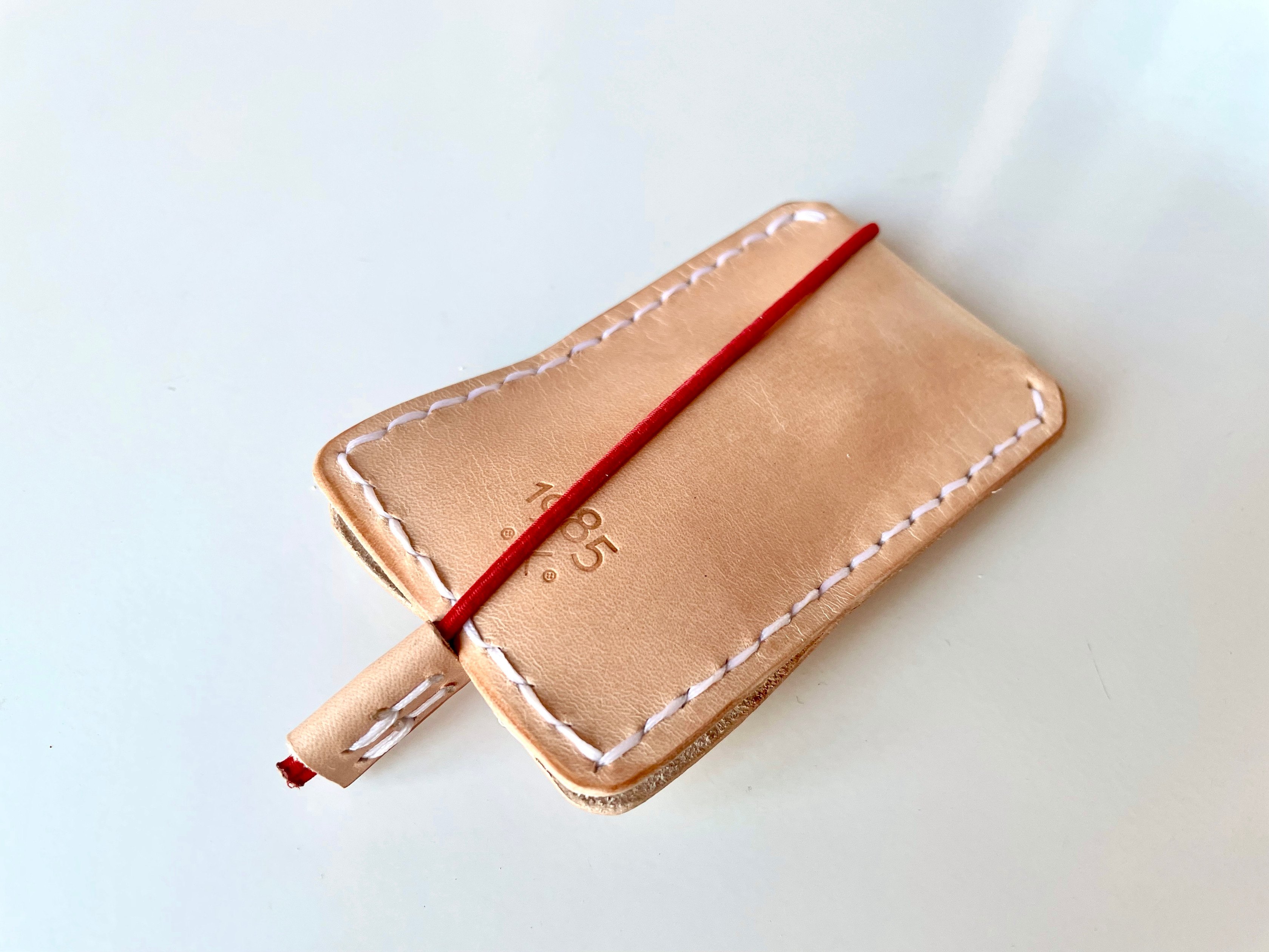 Slim key case by 1985 Studio closed, its red elastic cord wrapped across the vegetable-tanned leather and the 1985 mark